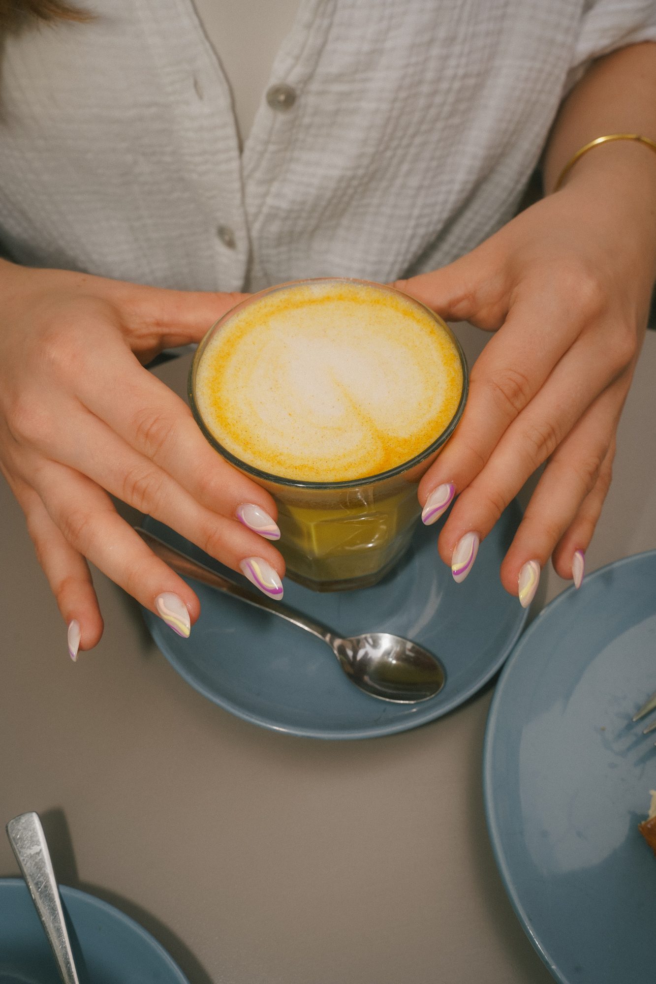 Gepflegte Hände mit hellen Nägeln halten einen Latte Macchiato