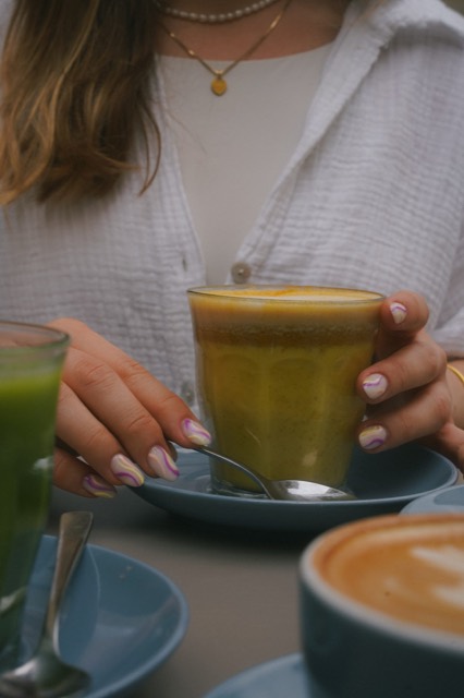 Hände mit zarten Nägeln halten ein Glas Chai